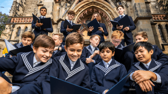 A candid gathering of boy choristers in their traditional blue uniforms holding blue choir folders on the steps of St. Thomas Church, Leipzig.
