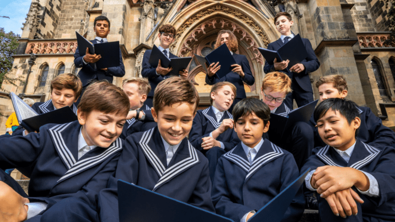A candid gathering of boy choristers in their traditional blue uniforms holding blue choir folders on the steps of St. Thomas Church, Leipzig.