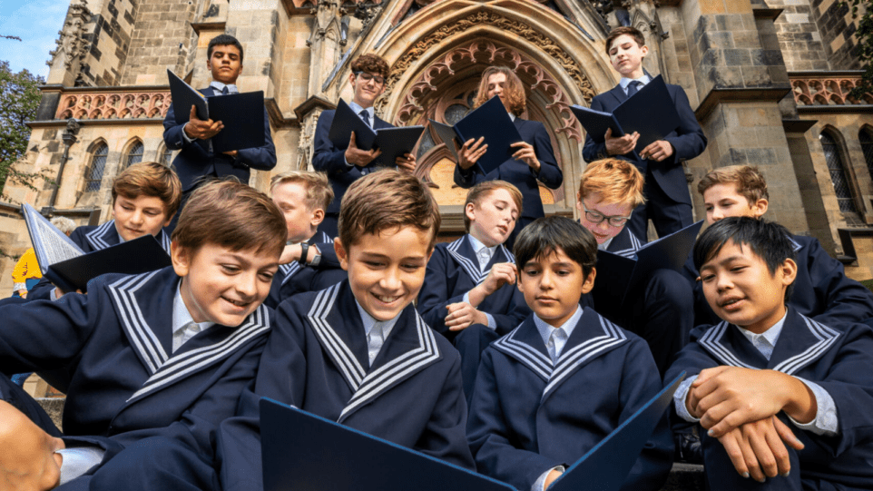 A candid gathering of boy choristers in their traditional blue uniforms holding blue choir folders on the steps of St. Thomas Church, Leipzig.