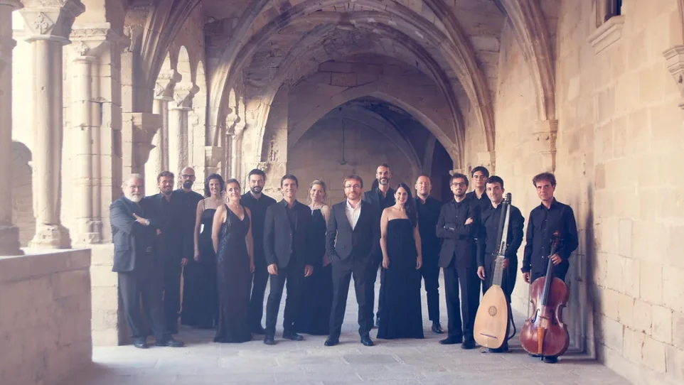 a group of well-dressed men and women, pne witha theorbo amd one wth a cello, pose in a stone passageway
