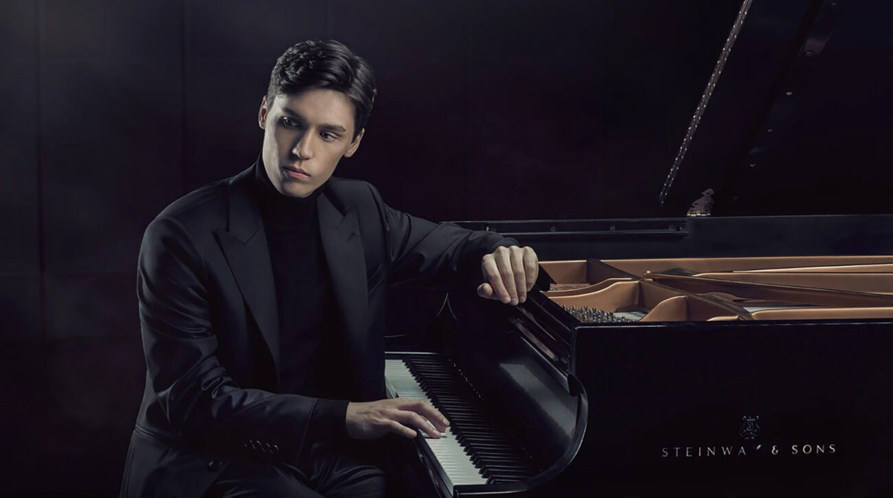 Young man in dark suit and mockneck plays piano