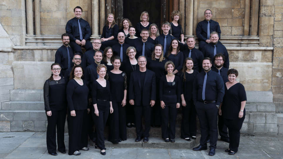 Conductor Jeff Hunt flanked by 30 members of St. Charles Singers in black concert attire posed in front of St. John the Baptist Church, Windsor. Windsor Church,
