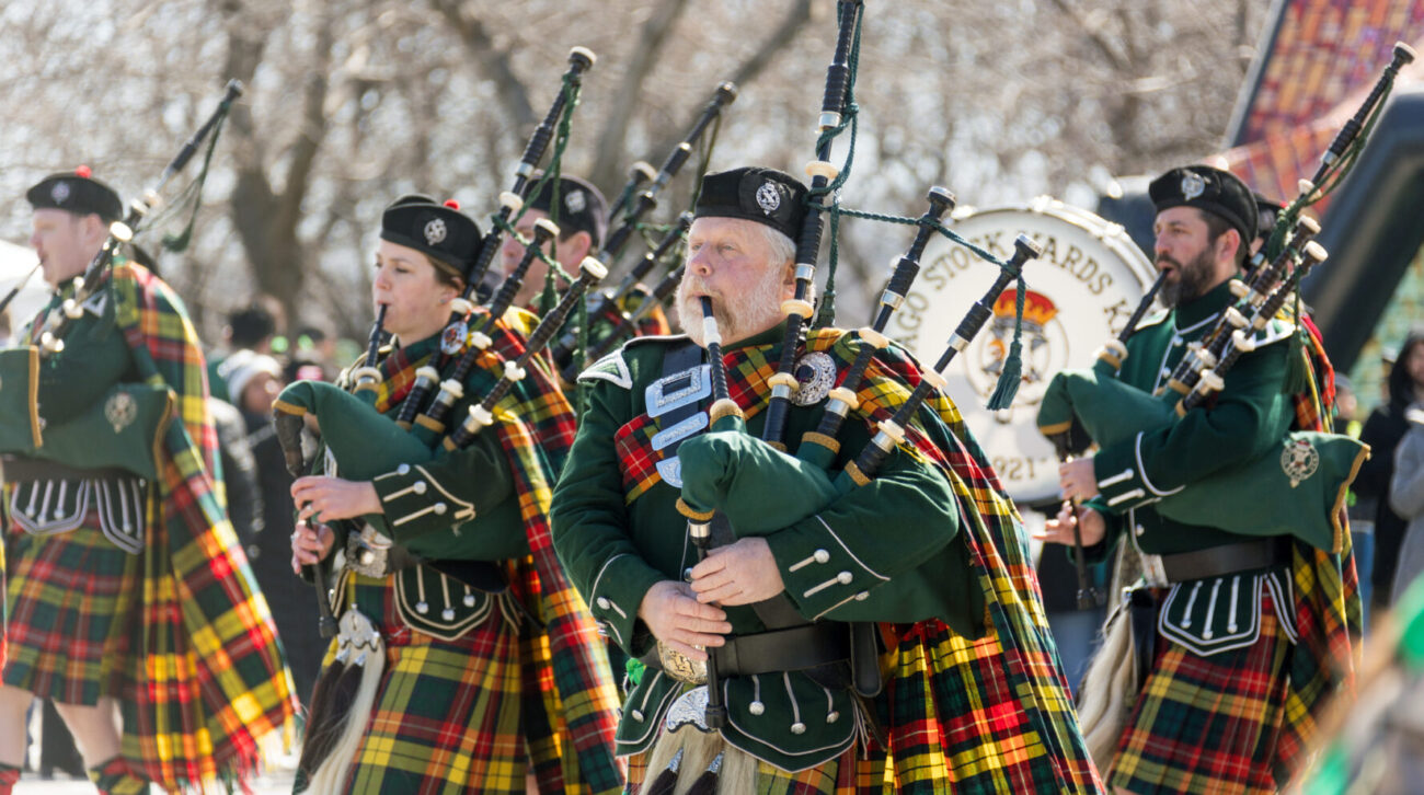 Bagpipe players walk down the street performing on a sunny day for St Patrick's Day