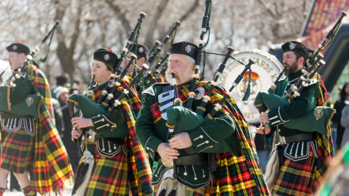 Bagpipe players walk down the street performing on a sunny day for St Patrick's Day