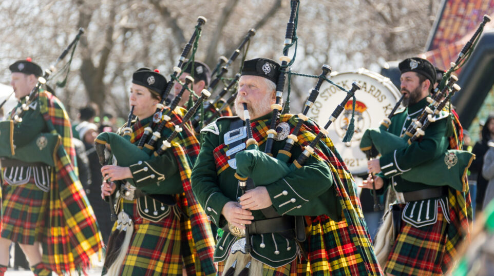 Bagpipe players walk down the street performing on a sunny day for St Patrick's Day