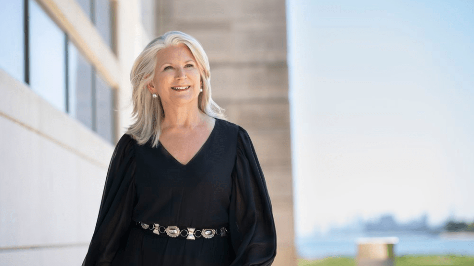 Patrice Michaels, smiling and looking upwards, in a belted, blousy black dress on the lakeside campus of Bienen School of Music.