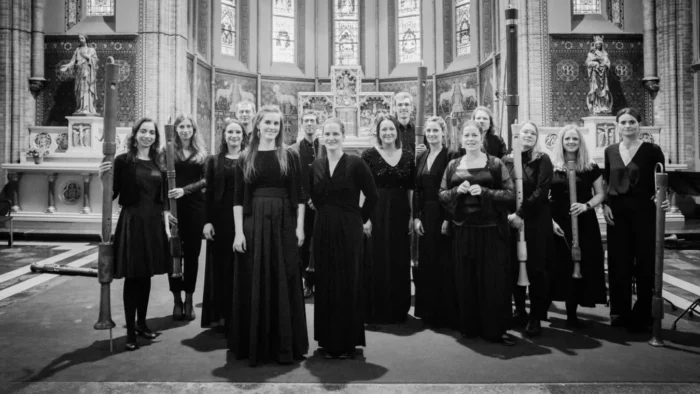 15 musicians, mostly women, in concert black pose in the apse of a church. Some are holding tenor, bass, and great bass recorders