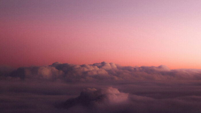 A golden hour pink hue image of the sky with some fluffy clouds