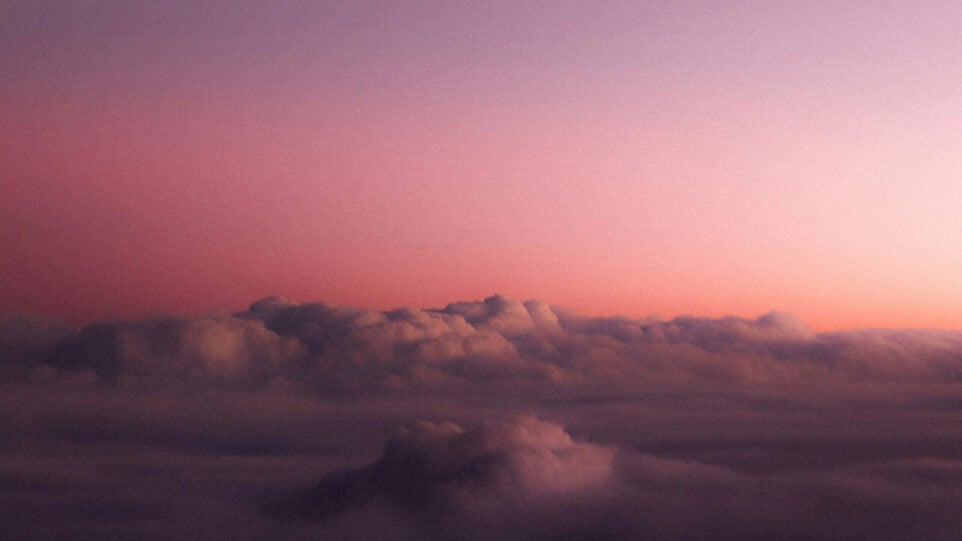 A golden hour pink hue image of the sky with some fluffy clouds
