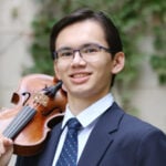 young man with suit and violin against ivy-clad stone wall