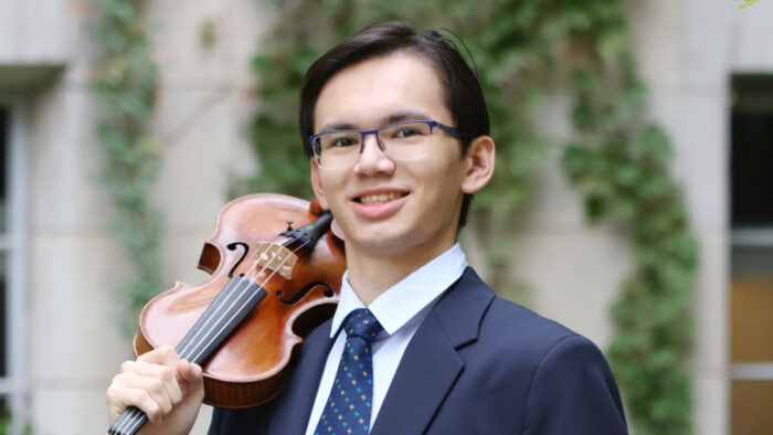 young man with suit and violin against ivy-clad stone wall