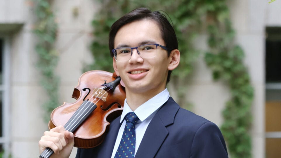 young man with suit and violin against ivy-clad stone wall