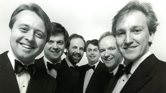 Group of six men in tuxedos grin towards the camera