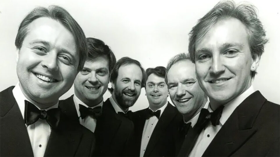 Group of six men in tuxedos grin towards the camera
