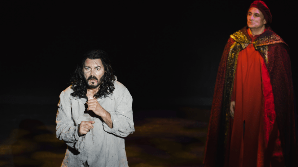 Franco Pomponi in the foreground as the prisoner, in distress, wearing tattered long sleeve prisoner garment. David Cangelosi in the background as the Grand Inquisitor in full red regalia.