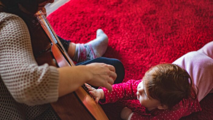 adult woman strums guitar as crawling baby puts hand on guitar