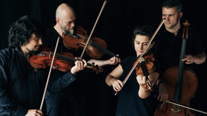 Black clad quartet play together in front of black background