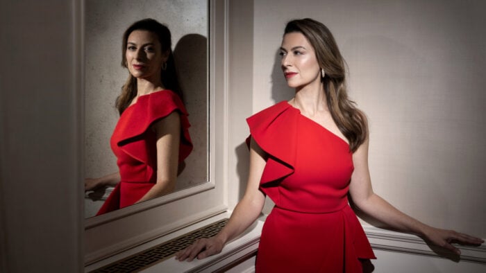 Woman in red dress gazes through mirror in moody-lit room