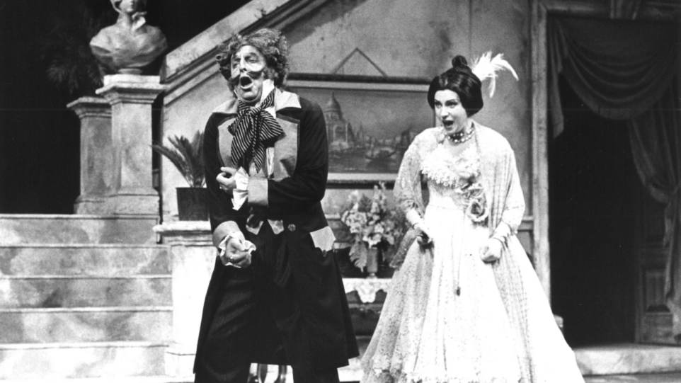 Black and white production photo of Don Pasquale (Peter Strummer) being chided by Norina (Sheri Greenawald) in period costumes.