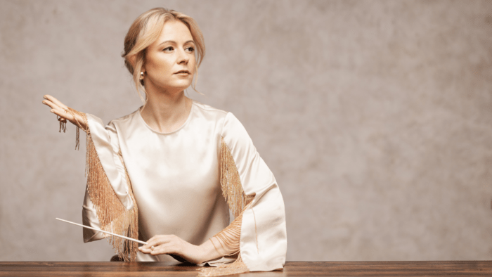 Stylized portrait of Gemma New in ivory/gold palette; New in left side of composition, staring mid-distance to the right, right hand extended lifting the fringed sleeve of her blouse, left hand resting on wood surface holding baton.