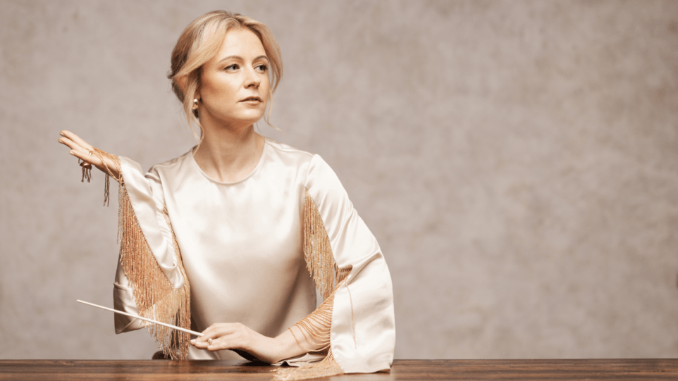 Stylized portrait of Gemma New in ivory/gold palette; New in left side of composition, staring mid-distance to the right, right hand extended lifting the fringed sleeve of her blouse, left hand resting on wood surface holding baton.
