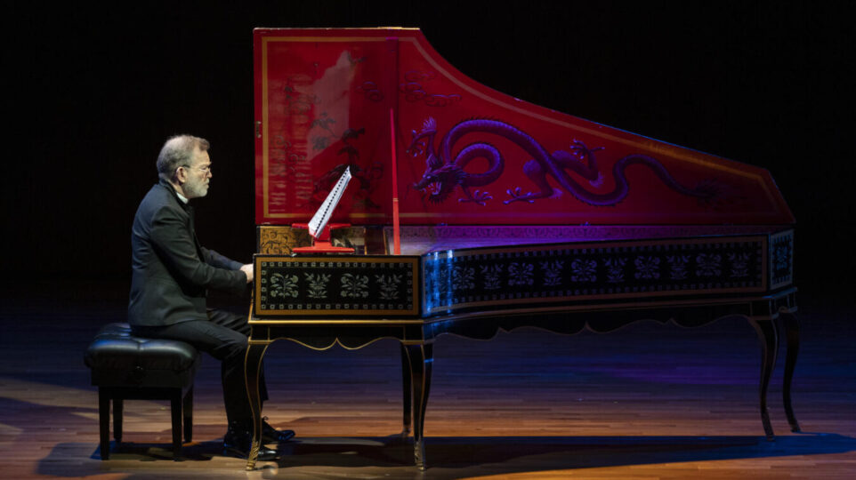 Christophe Rousset reads music and plays, seated at an ornately decorated harpsichord.