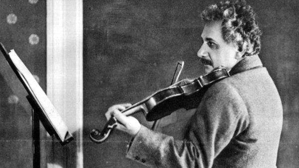 Albert Einstein in coat plays violin studiously in archival photo