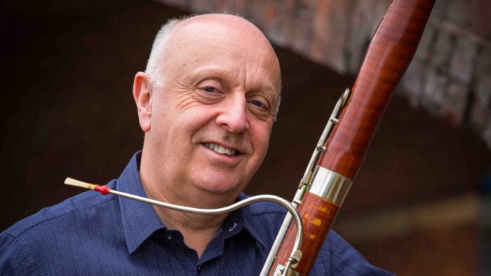 Man in Blue Shirt poses alongside a bridge with a bassoon