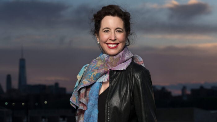 woman in leather jacket and colorful scarf in front of dusk city skyline
