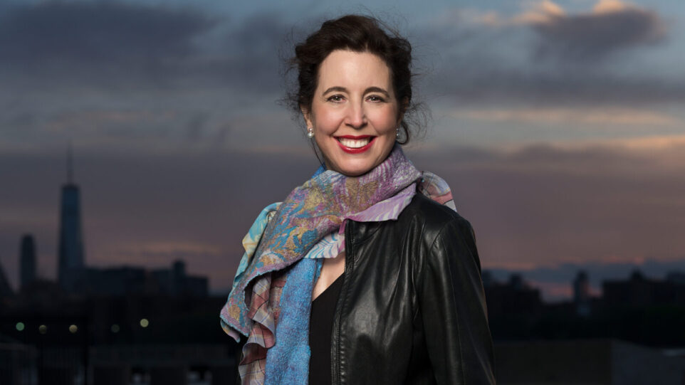 woman in leather jacket and colorful scarf in front of dusk city skyline