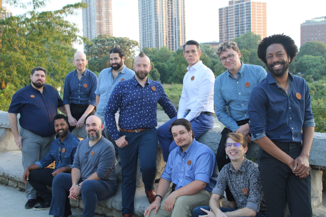 Members of the Constellation Men's Ensemble pose outdoors at a park with buildings behind them