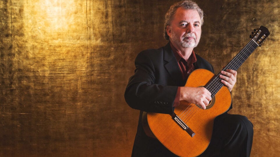 Man with guitar in front of shiny golden background