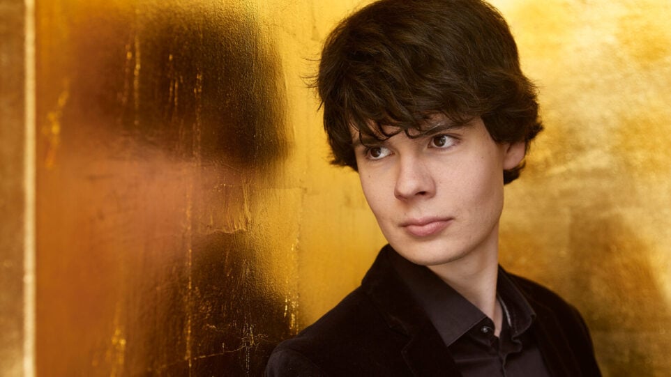 young man in black suit in front of gold leafed wall