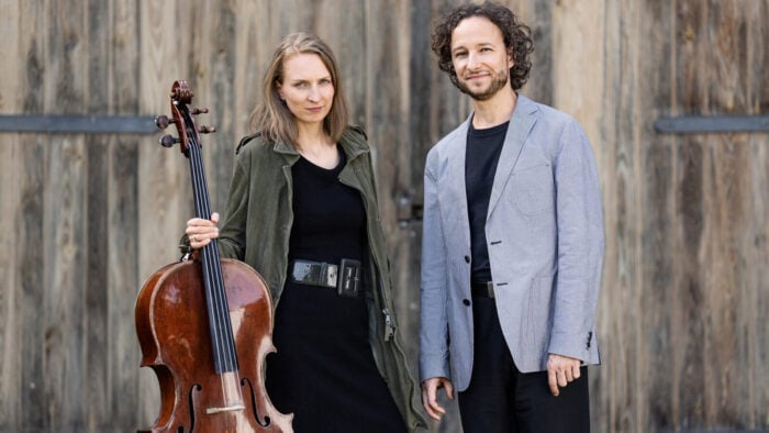 woman holding cello and man pose in front of rustic wood background