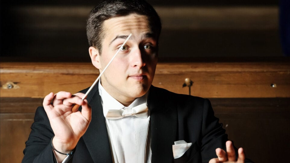 Conductor in white tie holds baton