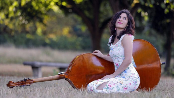 Woman sits in meadow with double bass