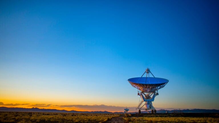 large satellite dish at sunrise with inky blue and bright orange sky