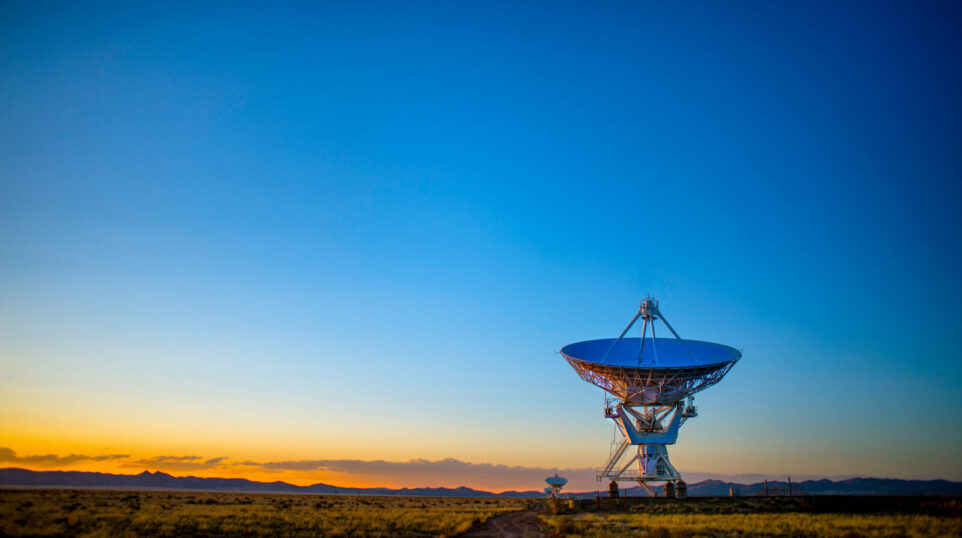 large satellite dish at sunrise with inky blue and bright orange sky