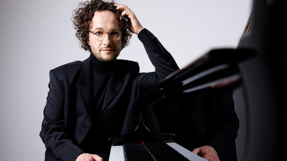 Man in dark suit leans against grand piano