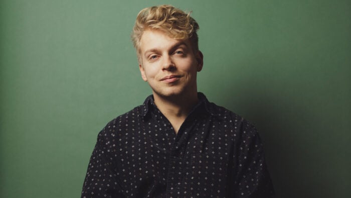 Man smiles casually in front of green backdrop