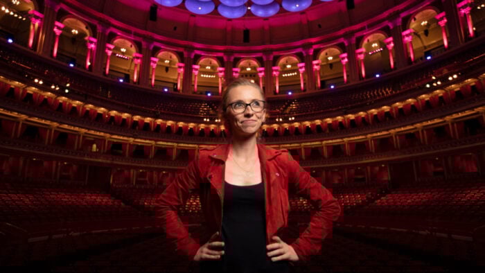 A woman in a red jacket in a grand red and purple lit performance hall