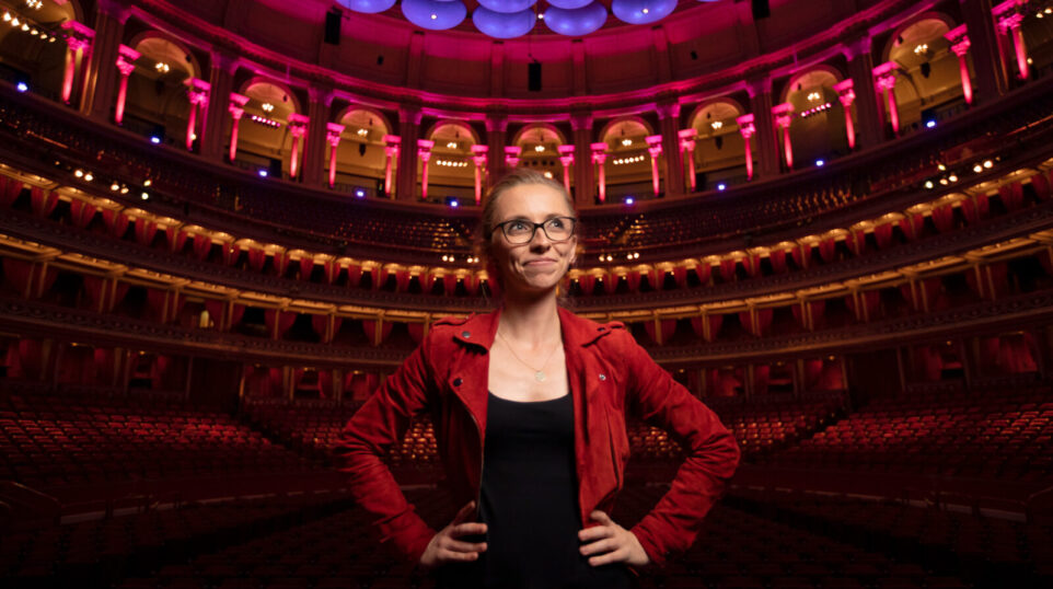 A woman in a red jacket in a grand red and purple lit performance hall