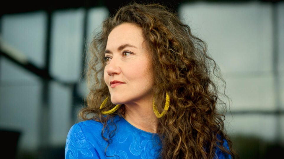 Woman smiles in vibrant blue dress and yellow colored hoop earrings
