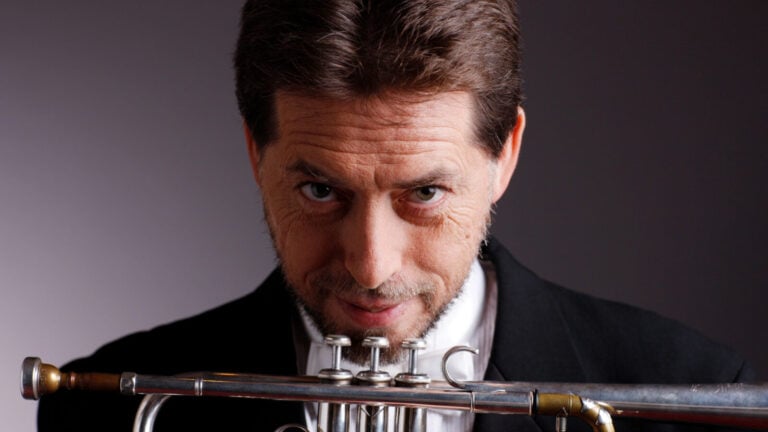 Man in suit holds trumpet and stares at camera