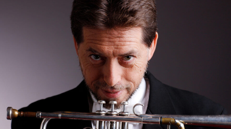 Man in suit holds trumpet and stares at camera