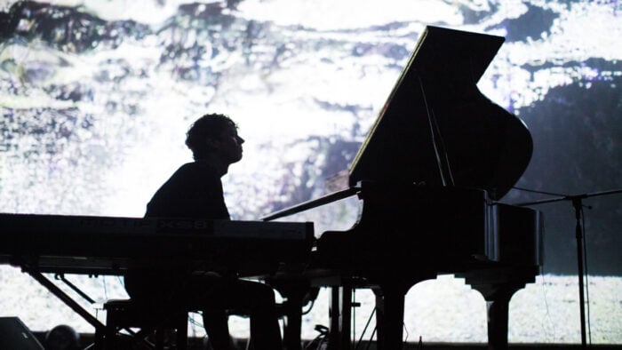 silhouette of man playing piano onstage with projection of landscape behind
