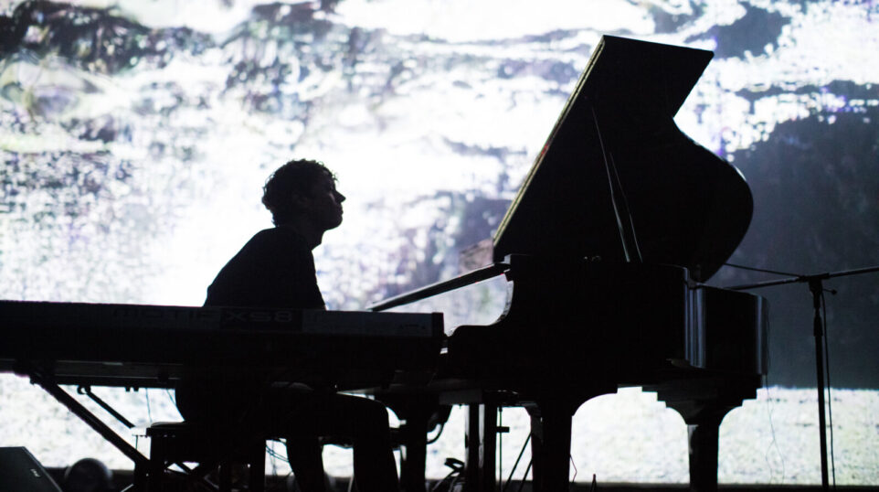 silhouette of man playing piano onstage with projection of landscape behind