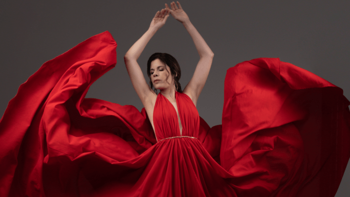 Ana María Martínez in a flowing red gown, skirt in motion as if just released by hands; in dancer's fifth position en haut.