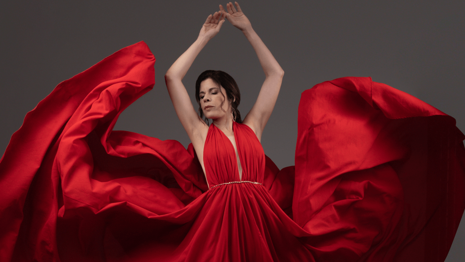 Ana María Martínez in a flowing red gown, skirt in motion as if just released by hands; in dancer's fifth position en haut.