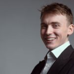 young man in suit grins widely
